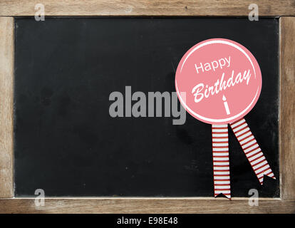 Happy Birthday Rosette mit festlichen gestreiften Bändern auf einem Vintage Kinder Schule Schiefer mit einem Holzrahmen und leere schwarze Oberfläche mit Exemplar für Ihren text Stockfoto