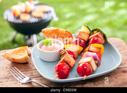 Gesunden Sommer essen Halloumi und Gemüse Kebabs geröstet über ein Outdoor-Grill im Garten und serviert mit einer pikanten Sauce und geröstetem Baguette auf einem Picknick-Tisch Stockfoto