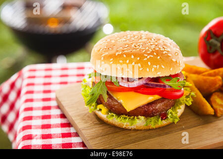 Leckeren Cheeseburger mit geschmolzenem Cheddar-Käse tropft über ground Beef-Burger mit frischem Salatzutaten garniert und serviert auf einem Holztisch auf ein Picknick im freien Tisch Stockfoto