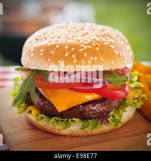 Leckere Burger mit Käse überbacken und einem dicken saftigen Boden Rindfleisch Patty, garniert mit Salat, Tomate, Zwiebel und Rucola auf einer Sesam Brötchen auf einem Picknick-Tisch im Garten steht Stockfoto