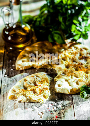 Italienische Focaccia Brot zu essen, eine hohe Gluten Ovenbaked Fladenbrot, gewürzt mit Olivenöl und Kräutern, serviert auf einem rustikalen Holztisch Stockfoto