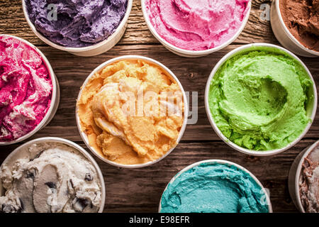 Auswahl an verschiedenen aromatisierte bunt Eis in Plastikwannen angezeigt auf einem alten Holztisch an einer Eisdiele für köstliche gefrorene Snacks an einem heißen Sommertag Stockfoto