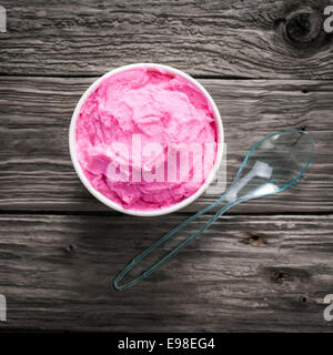 Draufsicht auf eine Wanne mit köstlich erfrischendes Rosa Eis mit einem Plastiklöffel für einen coolen Sommer-Snack an einem heißen Tag, quadratische Stockfoto
