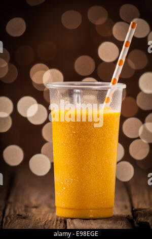 Glas gesunde erfrischende kalte orange Mango-Smoothie mit einem Strohhalm auf einer hölzernen Theke mit einer festlichen funkelnden Bokeh der Partei Stockfoto