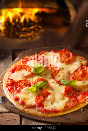 Leckere italienische Pizza mit geschmolzenem Käse und Tomaten in einer Pizzeria mit dem Feuer aus dem Ofen sichtbar hinter Stockfoto