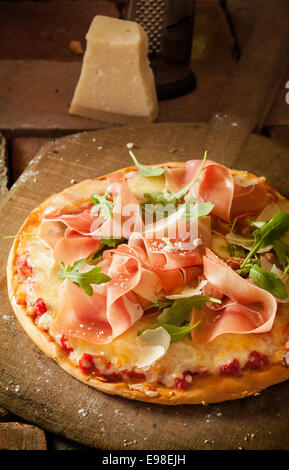 Erhöhte Ansicht einer ganzen italienischen Pizza belegt mit dünn geschnittenen Schinken und Rucola grüne Blätter Stockfoto