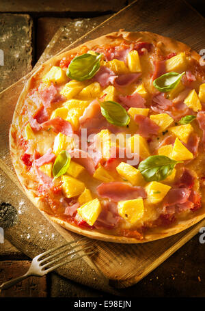 Erhöhte Ansicht eines exotischen Schinken und Ananas Pizza auf eine knackige Kruste serviert auf einem Holzbrett Stockfoto