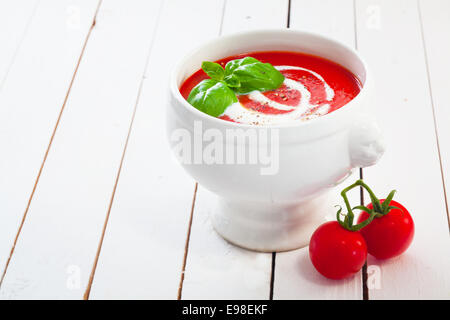 Schale mit leckeren roten Tomatensuppe und Sahne garniert mit Basilikum und Pfeffer auf bemalten Tafeln mit Exemplar Stockfoto