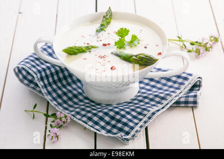 Creme von Spargelsuppe mit frischen grünen Spargelspitzen und gewürzt mit Gewürzen serviert in einer Schale auf einem blau-weißen aufgegebenes Tuch Stockfoto