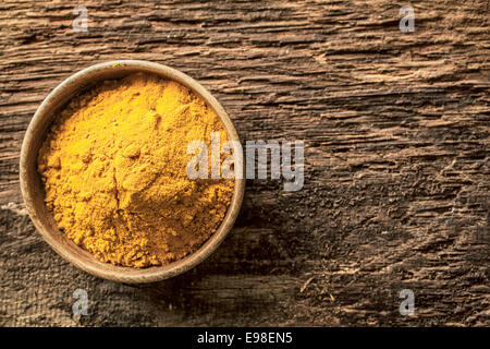 Asiatische Curry-Pulver, hergestellt aus einer Mischung von Gewürzen mit einem Masala oder Kurkuma Basis in einer kleinen Schüssel auf einer Grunge Strukturierte Holzoberfläche, Draufsicht mit Exemplar Stockfoto