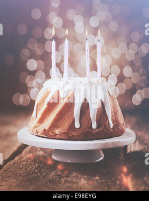 Retro-Vintage-Effekt Geburtstagskuchen glasiert mit weißen Zuckerguss verziert mit Perlen und gekrönt mit vier brennenden Kerzen der Partei mit einem Hintergrund Bokeh von funkelnden Lichtern tropft Stockfoto