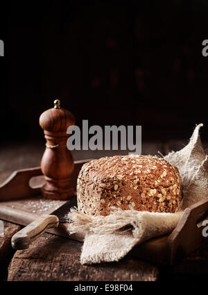 Frisch gebackene Land Samen Brot Vollkornbrot serviert auf einer Serviette und Tablett aus Holz mit Holz Pfeffermühle und Messer, Hochformat mit Exemplar Stockfoto