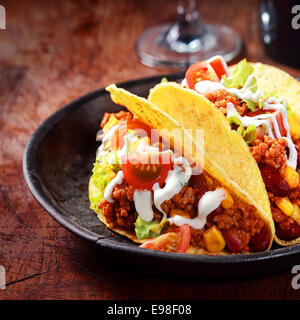 Knusprig goldene Mais-Tortilla oder Taco gefüllt mit Fleisch, Salat und Gemüse und beträufelt mit der sauren Sahne oder Mayo serviert in einer rustikalen Holzschale Nahaufnahme der Füllung Stockfoto