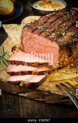 Seite des saftigen selten Roastbeef mit gemischten Kräutern und Gewürzen gewürzt geschnitzt in Scheiben auf einem rustikalen Holzbrett in einem Land Stockfoto