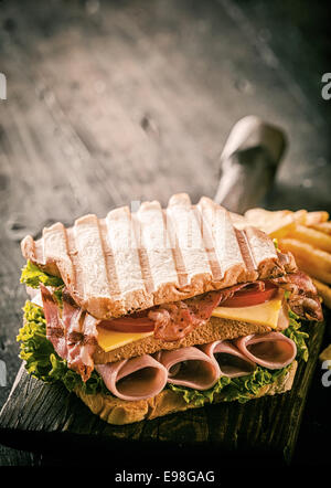 Gesunden gegrillten Schinken, Käse und Salat Sandwich Doppeldecker Formular auf getoastetem Weißbrot serviert auf einem alten Holzbrett auf einem rustikalen Holztisch mit Exemplar Stockfoto