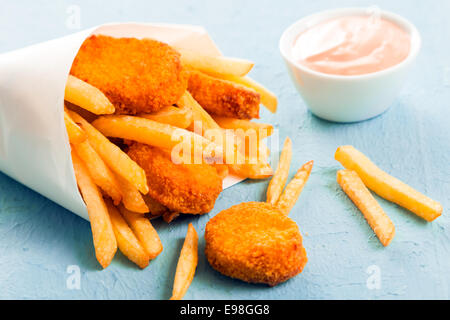 Gebratener Fisch-Nuggets mit goldene Pommes frites aus einem Papier-Membran aus einem Imbiss Fischgeschäft auf eine blaue Fläche, Nahaufnahme Stockfoto