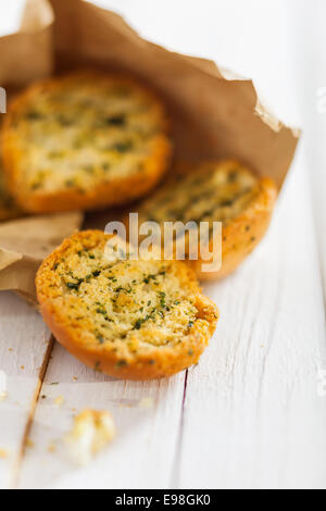 Frische knusprige Golden geröstet oder gegrillte Kräuter-Brötchen oder Scheiben Baguette frisch vom Grill in einem rustikalen braunen Papier-Paket auf einem weißen Picknick-Tisch Stockfoto