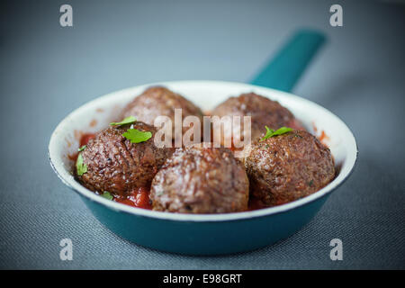 Nahaufnahme von lecker Würzige Frikadellen abgeschmeckt mit frischen Kräutern und einer Tomatensauce serviert, mit flachen Dof in einem blauen Topf Stockfoto