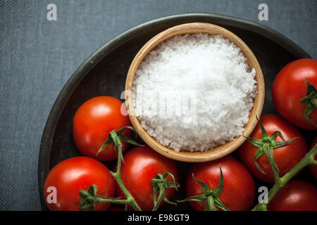 Blick von oben auf eine Schüssel mit groben natürliche Meer- oder Steinsalz für das Kochen mit frischen Reife rote Cherry Tomaten auf einem Teller bereit für den Einsatz in der Küche Stockfoto