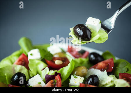 Genießen einen gesunden griechischen Salat Feta-Käse, Oliven, Tomaten und grünen grün mit einer Gabel über den Teller mit Salat, Feta und Oliven drauf aufgehängt Stockfoto