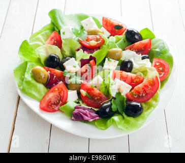 Mediterraner Salat mit Feta-Käse, Oliven, Salat, frischen Kräutern und Tomaten beträufelt mit Olivenöl für eine gesunde Ernährung, Stockfoto