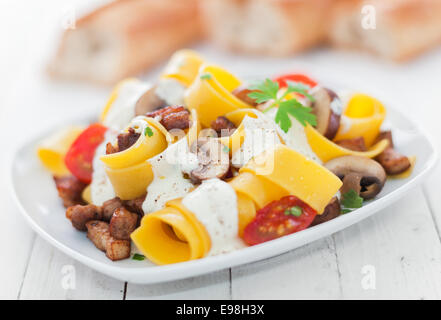 Italienische Eiernudeln mit Tomaten und Champignons beträufelt mit einer pikanten Kräuter-Sahne-Sauce für köstliche italienische Küche Stockfoto