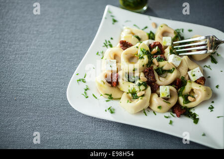 Ausschank von Feta-Käse, Basilikum und Pinienkernen-Pesto mit italienischen Tortellini Nudeln auf einem modernen geschwungenen weißen Teller über einem grauen Tuch Stockfoto