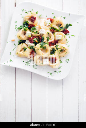 Tortellini Nudeln mit frischen Kräutern, würzig pikanten Sauce und Feta-Käse auf eine elegante Teller auf einem weißen Holztisch mit Exemplar Stockfoto