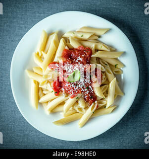 Traditionelle italienische Penne Vergangenheiten, garniert mit eine herzhaften würzigen Tomatensauce bestreut mit geriebenem Parmesan-Käse und garniert mit frischem Basilikum, Draufsicht Stockfoto