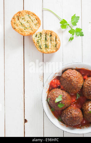 Pikante Rindfleisch Frikadellen in einer würzigen Tomatensauce mit frischen Kräutern, serviert in einem Topf mit knusprig goldene gegrillte Kräuter Brot und frischer Petersilie auf einem weißen hölzernen Tisch, Ansicht von oben Stockfoto