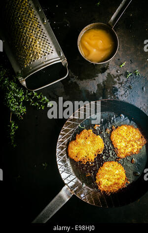 Köstliche frische Gebratene Kartoffel Krapfen hergestellt aus geriebenen Kartoffeln, frischen Kräutern und Ei in einer Landhausküche mit Vintage Reibeisen, Blick vom Overhead mit Zutaten Stockfoto