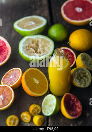 Frischen Zitronensaft in eine rustikale Küche mit einer Flasche Orangensaft Mischung umgeben von halbierten Orangen, Grapefruit, Blutorange, Limette und Zitrone vorbereiten, haben einige davon zusammengedrückt worden Stockfoto