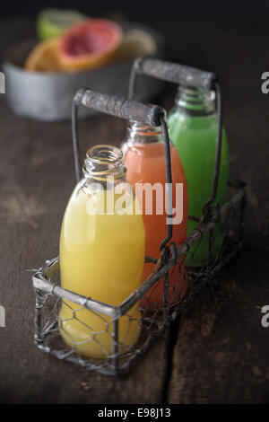 Glasflaschen von sortierten frische Fruchtsäfte in einem alten Metall und Draht-Rack in eine rustikale Küche mit Orange, Grapefruit und Zitrone Stockfoto