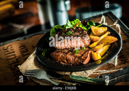 Gesunde schlanke gegrilltes Rindersteak Medium-rare und Gemüse mit gebratenem Kürbis und belaubte grüne Kraut Salat in einem urigen Pub oder Stockfoto