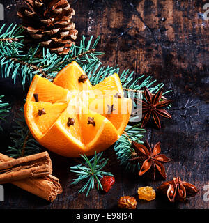 Weihnachten-Frucht und Würze-Hintergrund mit einem bunten Muster geschnitten Orange dekoriert mit Nelken eingebettet auf Kiefer Laub mit einem Kegel, Zimt, Sternanis und Muttern auf einer rustikalen Kulisse im quadratischen format Stockfoto