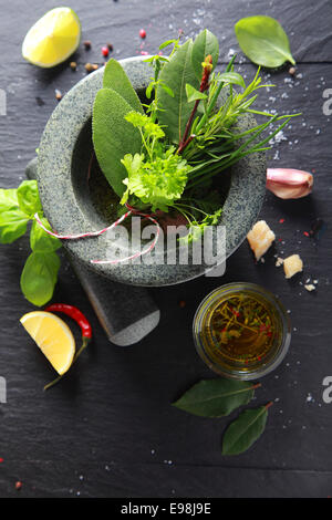 Verschiedene frische aromatische Küchenkräuter in einem Stößel und Mörser mit Knoblauch und gewürzten Olivenöl auf der Seite, Draufsicht auf Schiefer mit Exemplar Stockfoto