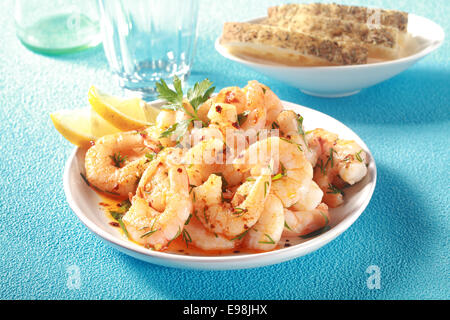 Gourmet Meeresfrüchte Vorspeise gegrillte rosa Garnelen oder Shrimps mit frischen Kräutern und Olivenöl gewürzt und garniert mit frischen Zitronenscheiben auf a blaue Tabelle Stockfoto