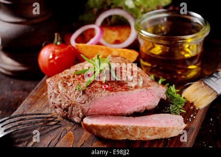 Zarte schlanke Medaillon von seltenen gegrilltes Rindersteak, gewürzt mit frischen Kräutern durch die Textur zeigen geschnitten und serviert mit frischem Gemüse auf eine rustikale Schneidbrett aus Holz Stockfoto