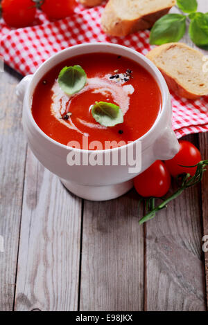 Hausgemachte Tomatensuppe, garniert mit Sahne und Basilikum auf einem rustikalen Holz Küchentisch mit Zutaten und Exemplar Schüssel Stockfoto