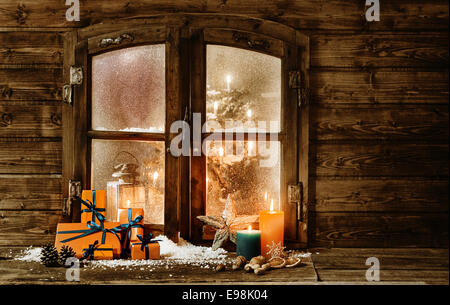 Festliche Weihnachten Kabine Holzfenster mit einer Geschenkverpackung bunt Orange präsentiert, brennende Kerzen und Dekorationen im Winterschnee und einen Einblick in ein geschmückter Weihnachtsbaum durch das mattierte Fenster Stockfoto