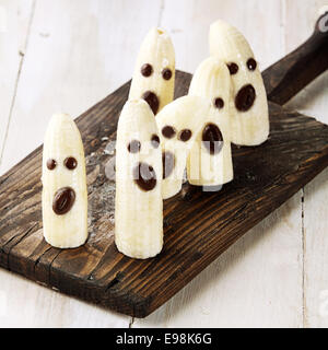 Banane Halloween Geister mit Schokolade Gesichter auf Holzbrett Stockfoto