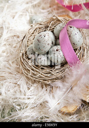 Blaue Ostereier in einem Nest auf Federn und eine rosa Schleife gesprenkelt Stockfoto