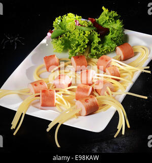 Heißer Snacks Hund Wiener und Nudel Halloween Spinne mit Salat-Garnitur auf weißer Teller auf schwarzem Hintergrund Stockfoto