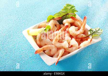 Gourmet-rosa Garnelen oder Shrimps Tails serviert in einer Schale mit Zitrone und frischen Kräutern für eine köstliche Meeresfrüchte Vorspeise zu einem Dinner, erhöhte Ansicht auf türkis-blau mit Exemplar Stockfoto