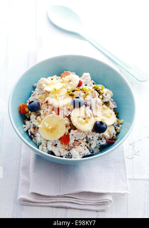 Vogelperspektive anzeigen einer Portion hausgemachtes Müsli, garniert mit getrockneten Früchten, Beeren, in Scheiben geschnittenen Bananen und Nüssen in einer blauen Schüssel auf eine Serviette bereit für ein gesundes, leckeres Frühstück Stockfoto