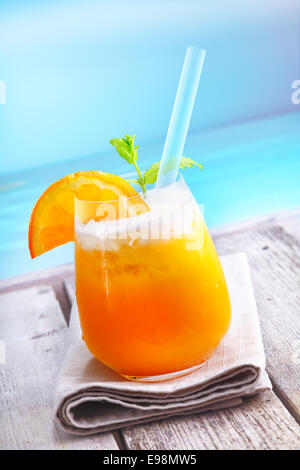 Erfrischender Eistee orange cocktail stehend auf einem Holzdeck mit Blick auf den Ozean auf Urlaub in einem tropischen resort Stockfoto