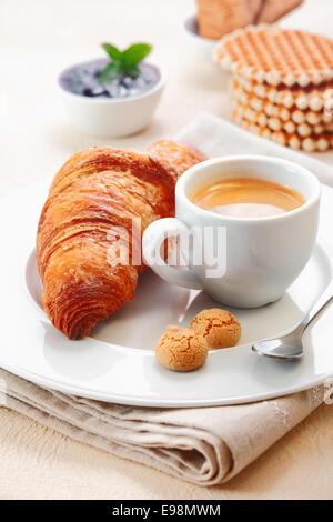 Frisch gebackene knusprig goldene Croissant mit einer Tasse reichen Espresso und zwei kleine Makronen Plätzchen in einem Restaurant serviert Stockfoto