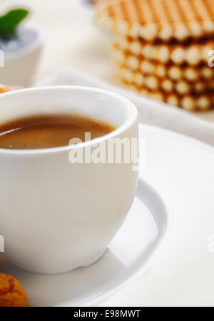 Detailansicht eines einfachen weißen Keramik Tasse mit reich gefüllt starken Espressokaffee mit Waffeln zum Frühstück serviert beschnitten Stockfoto