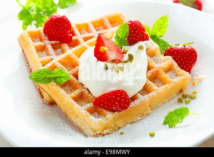 Goldene Waffeln garniert mit frischen in Scheiben geschnittenen Erdbeeren mit Sahne und bestreut mit Zucker für ein köstliches dessert Stockfoto