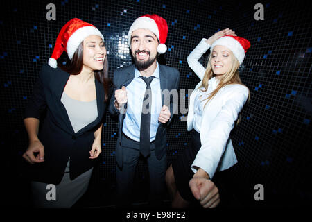 Porträt der fröhlichen Business Group in festlich gekleidet und Santa Caps Tanz im Nachtclub Stockfoto